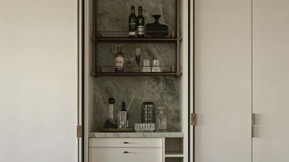 A home bar with a marble green backsplash and three shelving units as well as draws and a wine rack at the bottom. 