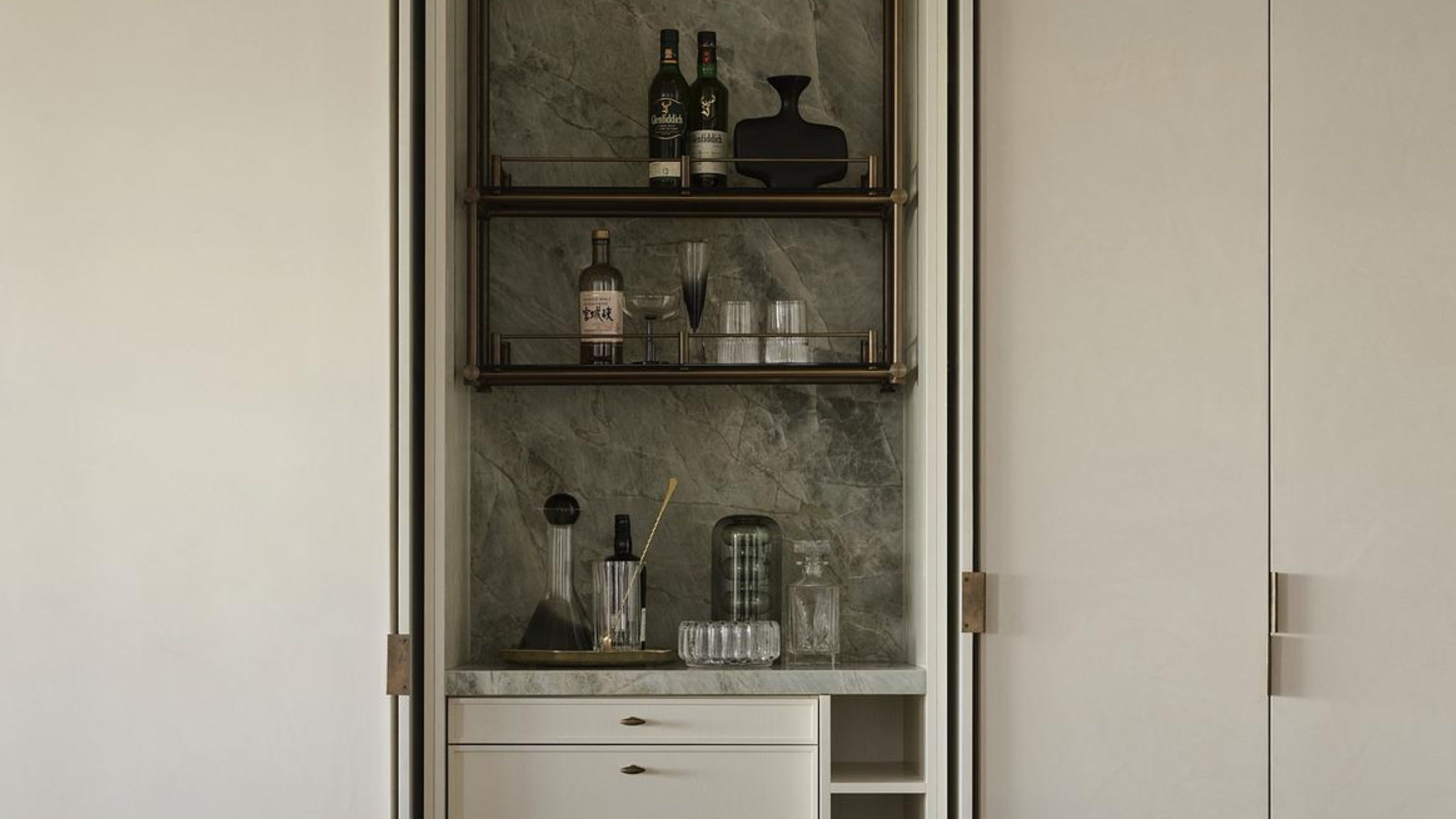 A home bar with a marble green backsplash and three shelving units as well as draws and a wine rack at the bottom. 