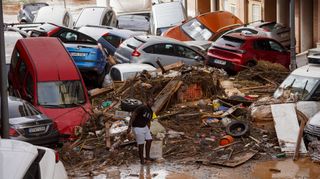 A boy clears debris in a flooded street filled with crashed cars