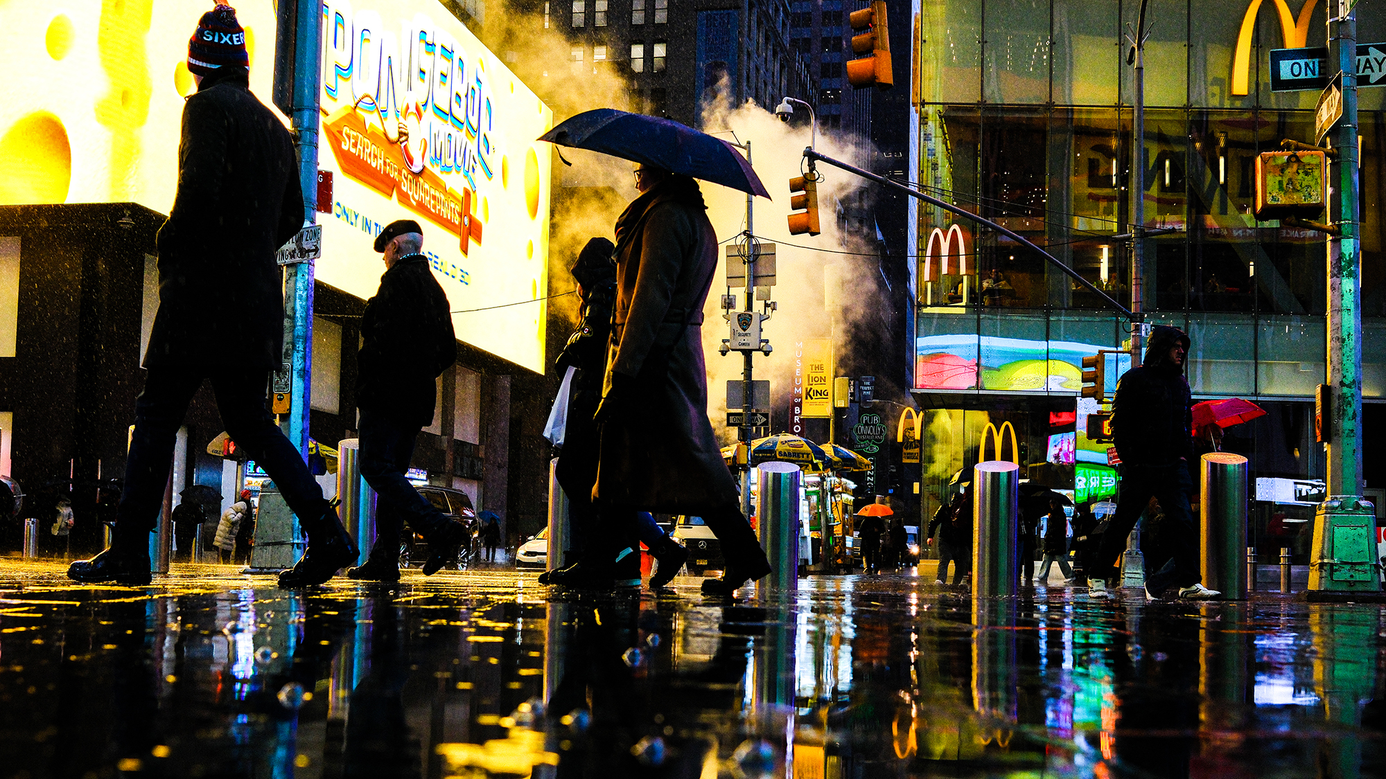 Pedestrians walk through rainy, neon-lit streets in Manhattan, New York City