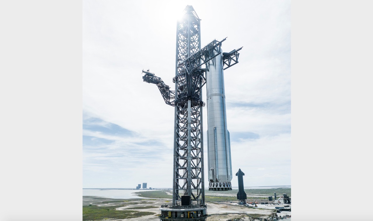 spacex tower lifting a big super heavy rocket on the launch pad. starship is far in the background