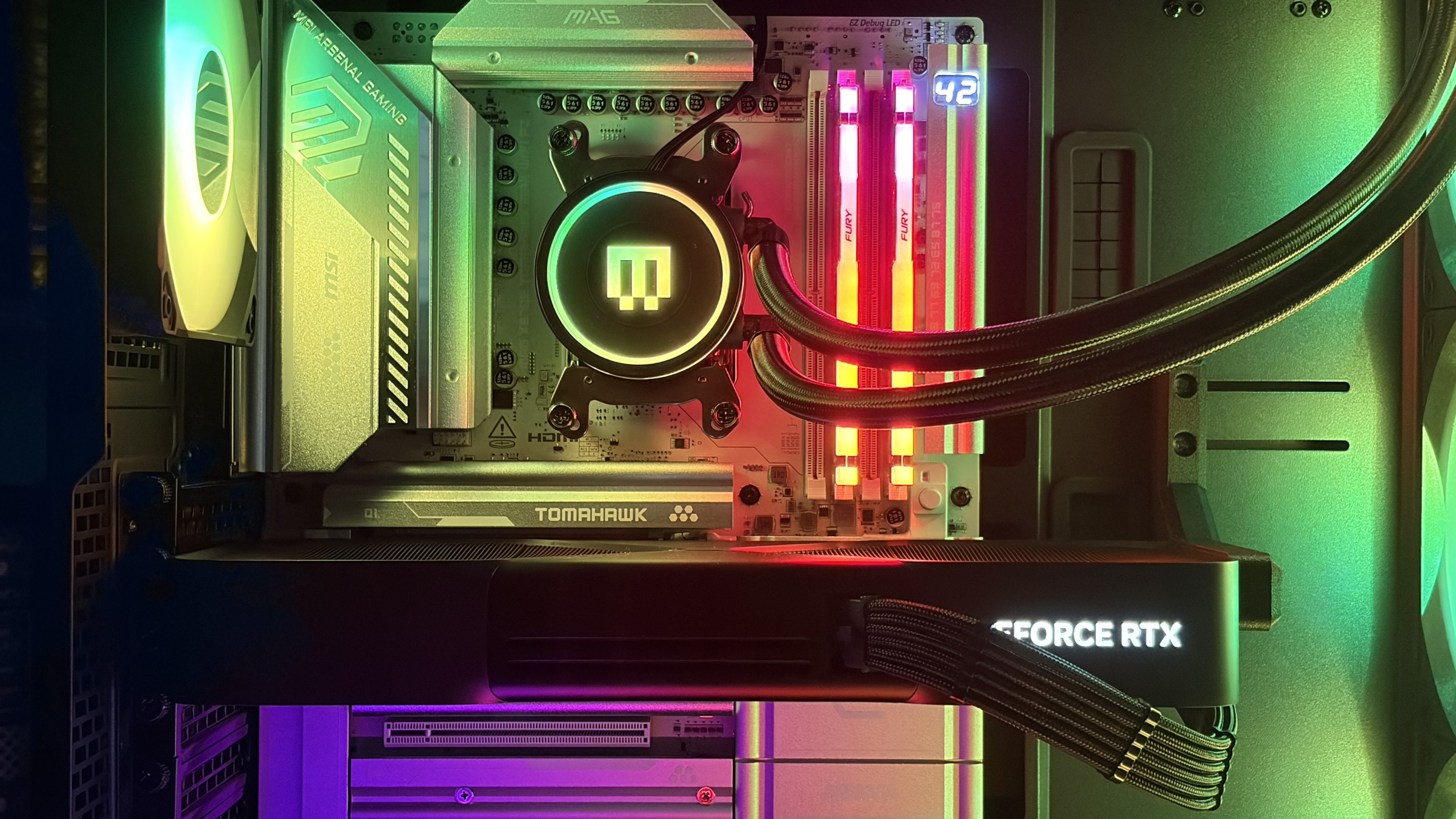 A colorful MG-1 MK.II computer interior showcasing a cooling system with RGB lighting, an MSI Tomahawk motherboard, and a lit GeForce RTX graphics card.