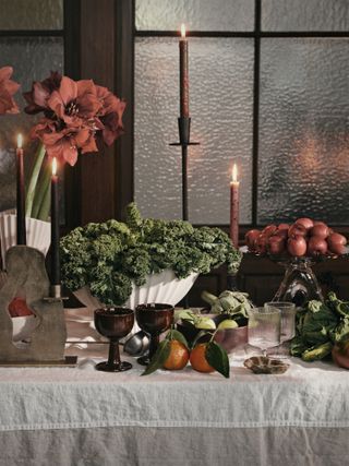 Christmas table decorated with dishes of fruit and leafy veg, dark wine glasses and white tablecloth