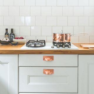 Hob in a white tiled kitchen, with a copper pot sitting on top. This matches the copper handles on the kitchen cupboards below