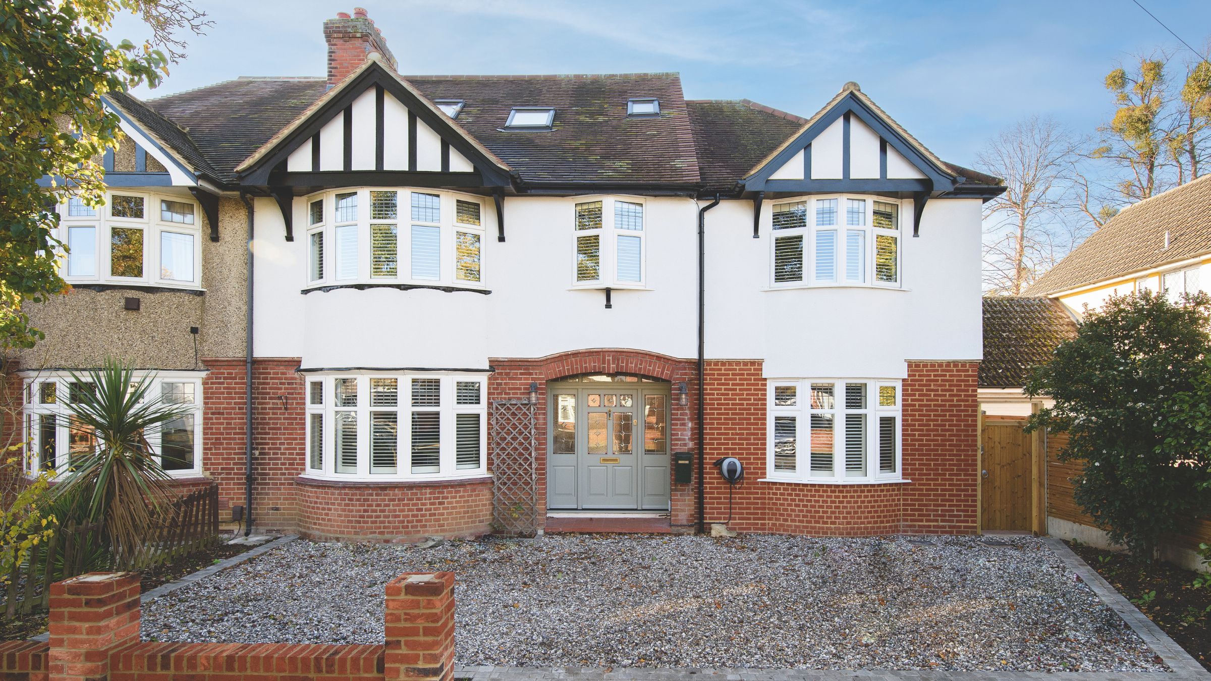 Brick semi-detached house with white render on top and brick on the bottom, with a large gravel driveway in front of it