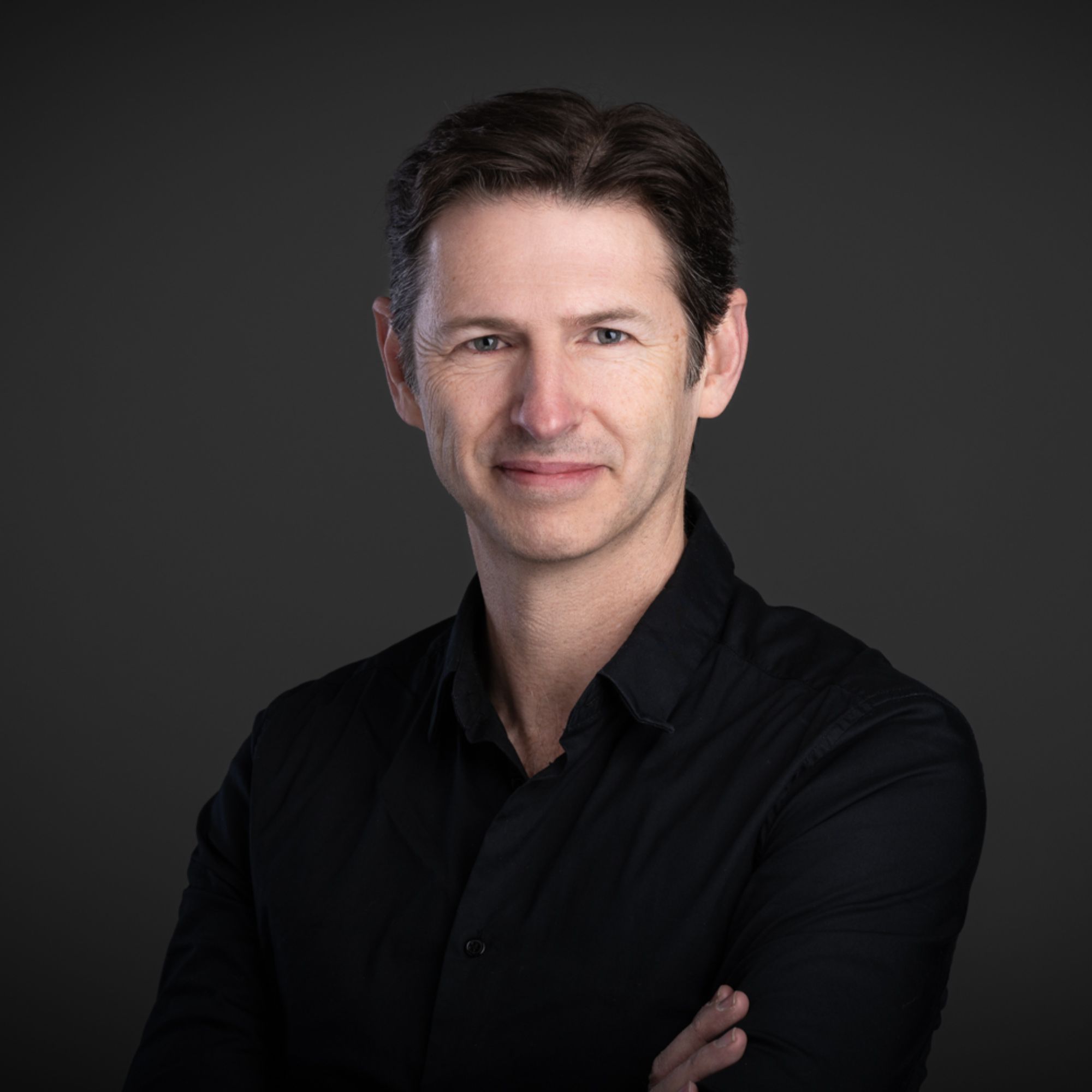 A headshot of Dr. Mike Gradisar wearing a black shirt against a dark grey background