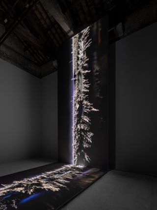 20-foot-tall multisensory sculpture with never-ending moving image on display on perpendicular screesns. Photographed in a dark room.