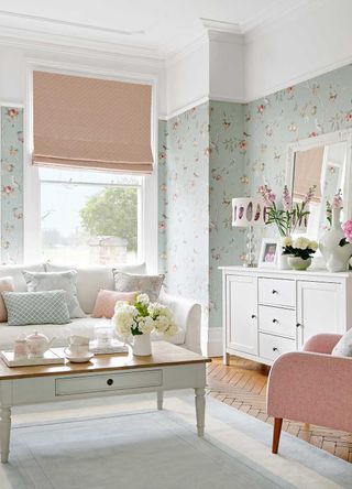 pastel living room with bird print wallpaper pink blind and a pink armchair with a white sofa and white painted coffee table