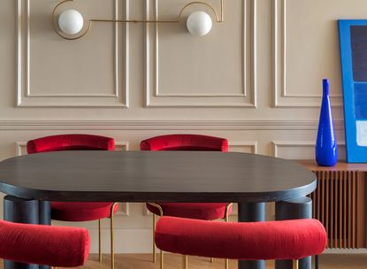 A dining room with wall paneling and red chairs