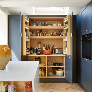 open pantry cupboard doors in a navy blue and white kitchen