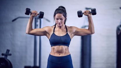 A woman performing dumbbell shoulder press in the gym