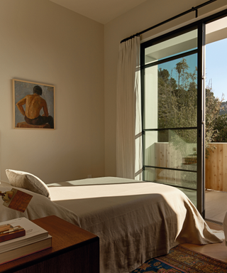 bedroom with neutral coloured bedding and art on walls and crittal window door eltting in light and balcony