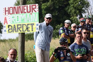 Spectators stand on the side of the road next to a placard reading "honor to Romain Bardet during the 3rd stage of the 77th edition of the Criterium du Dauphine cycling race, 207,2 km between Brioude and Charantonnay, on June 10, 2025. (Photo by Anne-Christine POUJOULAT / AFP)