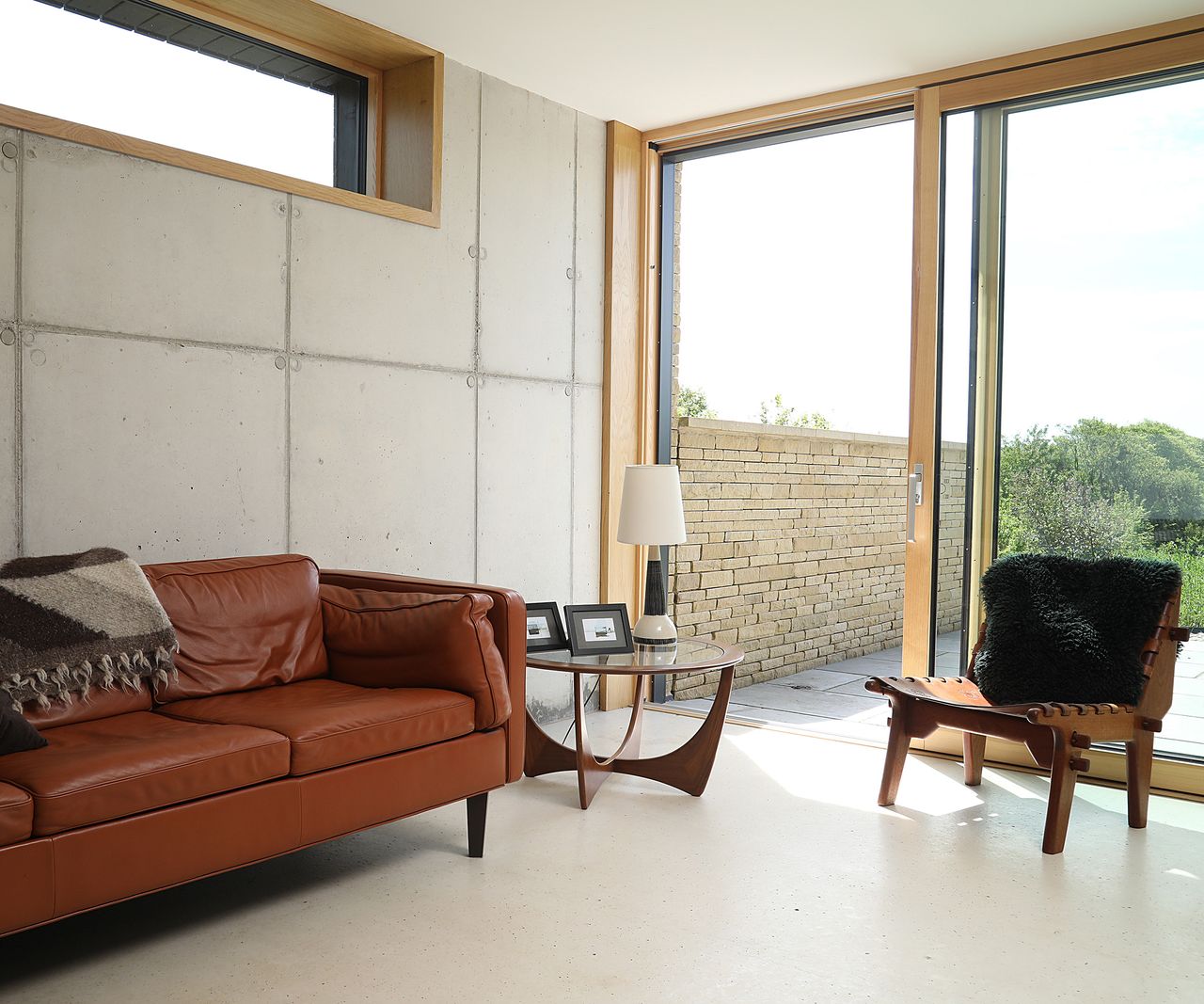 A rust brown leather sofa in a minimalist living room with sliding glazed doors leading out into the back garden of a contemporary self build home