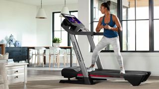 Image shows the ProForm Premier 900 treadmill in a living room being used by a woman.