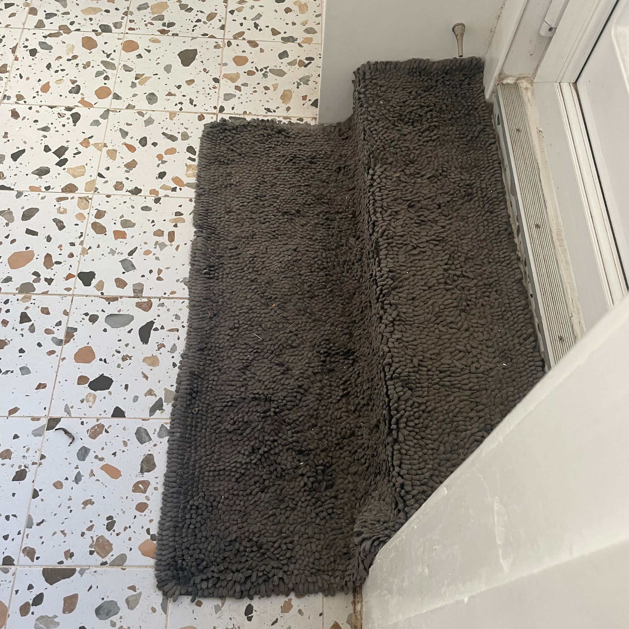 Dark grey Muddy Mat doormat by a white back door, in a kitchen with terrazzo tiled floors