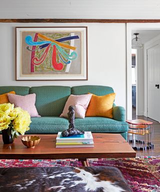 living room with green sofa, pink and orange cushions, wooden coffee table, kilim rug and cowhide bench