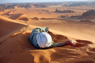 Sahara desert guide Moussa Macher rests on the summit of the largest dune in the Sahara called Tin-Merzouga. The dune is in the Tadrat region of the desert full of red sand.