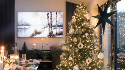 A dining room with a set table with a lit-up Christmas tree and curtain lights decorating windows