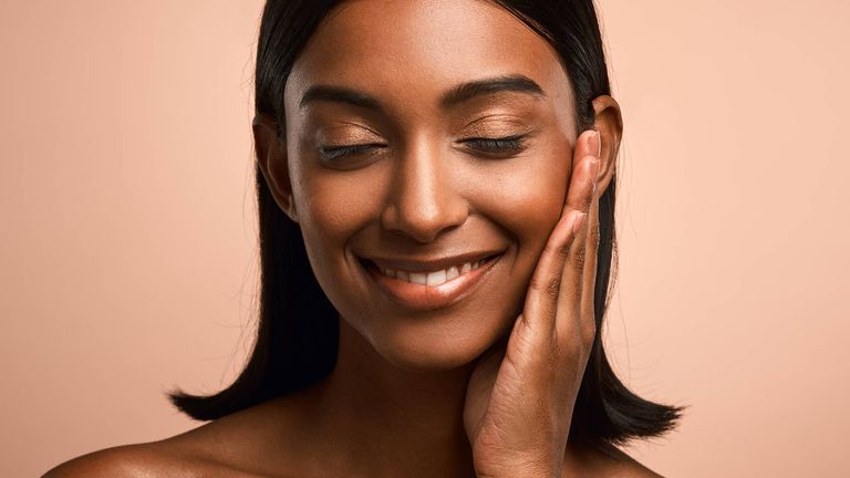 Shot of a beautiful young woman touching her face while posing against a brown background