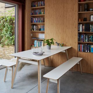 dining table with bench seating beside bifold doors and a wall of fitted timber storage with shelving and cupboards