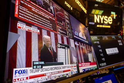 President Donald Trump speaking during a Rose Garden event on a TV screen with the New York Stock Exchange (NYSE) ticker boards surrounding it