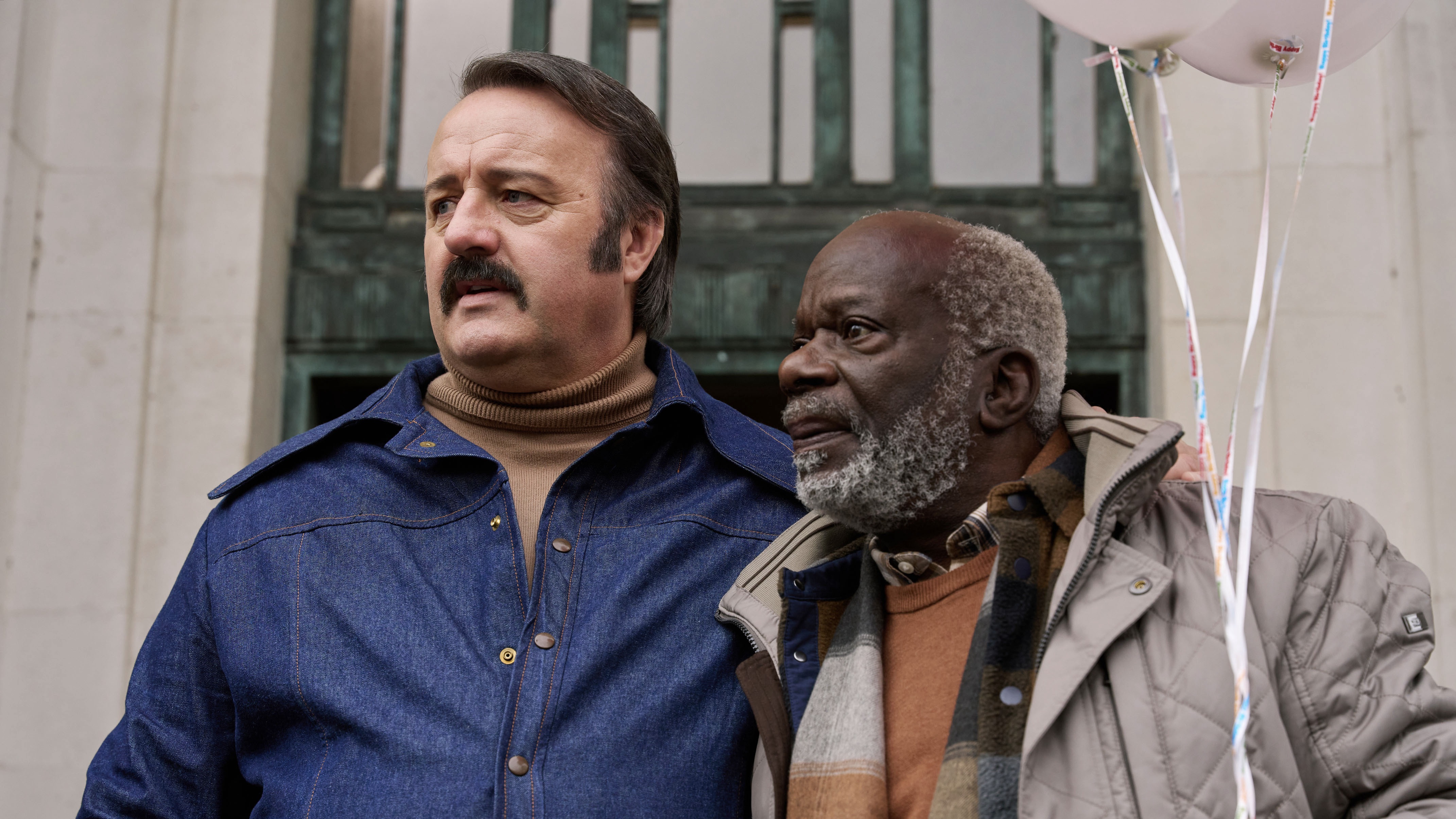 Tony Bubbins in a denim jacket as Mammoth and Joseph Marcell in a beige coat as Roger in Mammoth