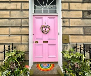 Front door of Miranda Jane Dickson's house painted a bright pink with a rainbow welcome carpet and heart shape wreath on the door