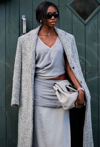a photo of a woman wearing a gray coat over a gray top and matching skirt with a designer bag