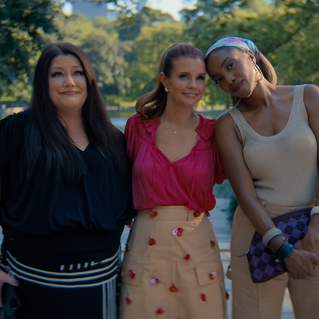 Brooke Elliott as Dana Sue Sullivan, JoAnna Garcia Swisher as Maddie Townsend, Heather Headley as Helen Decatur with their arms around each other in summer clothes smiling standing in a sunny central park in new york city
