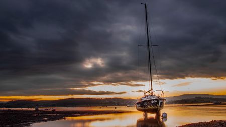 Sailing boat at low tide in front of moody sky with bright sunrise