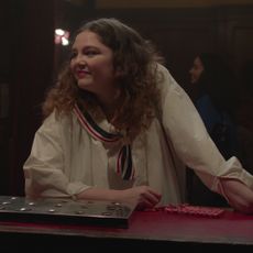 Jess in Too Much wears a white sailor dress with a lace skirt at a bar