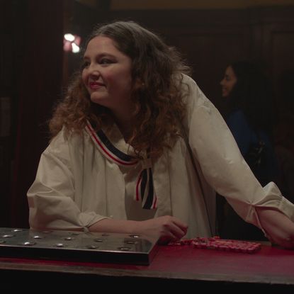 Jess in Too Much wears a white sailor dress with a lace skirt at a bar