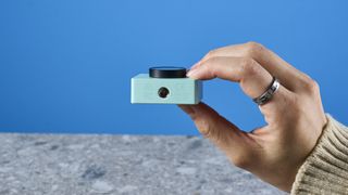 a photograph of a 1 inch wide mint webcam with a 4K sensor and built-in microphone, photographed against a blue background