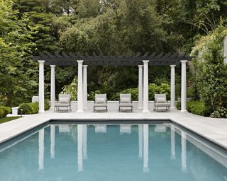 A swimming pool with columned black and white pergola and grey sun loungers