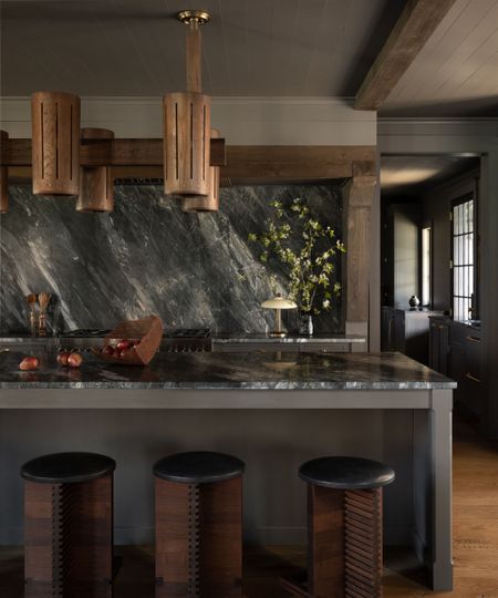 Modern farmhouse kitchen island with dark marble countertop, vintage wooden stools, and dramatic marble backsplash behind the range.