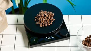 fellow tally pro coffee scale with a large circular weighing pad and coffee beans and an LED display with a dial and timer photographed against a blue tom's guide background