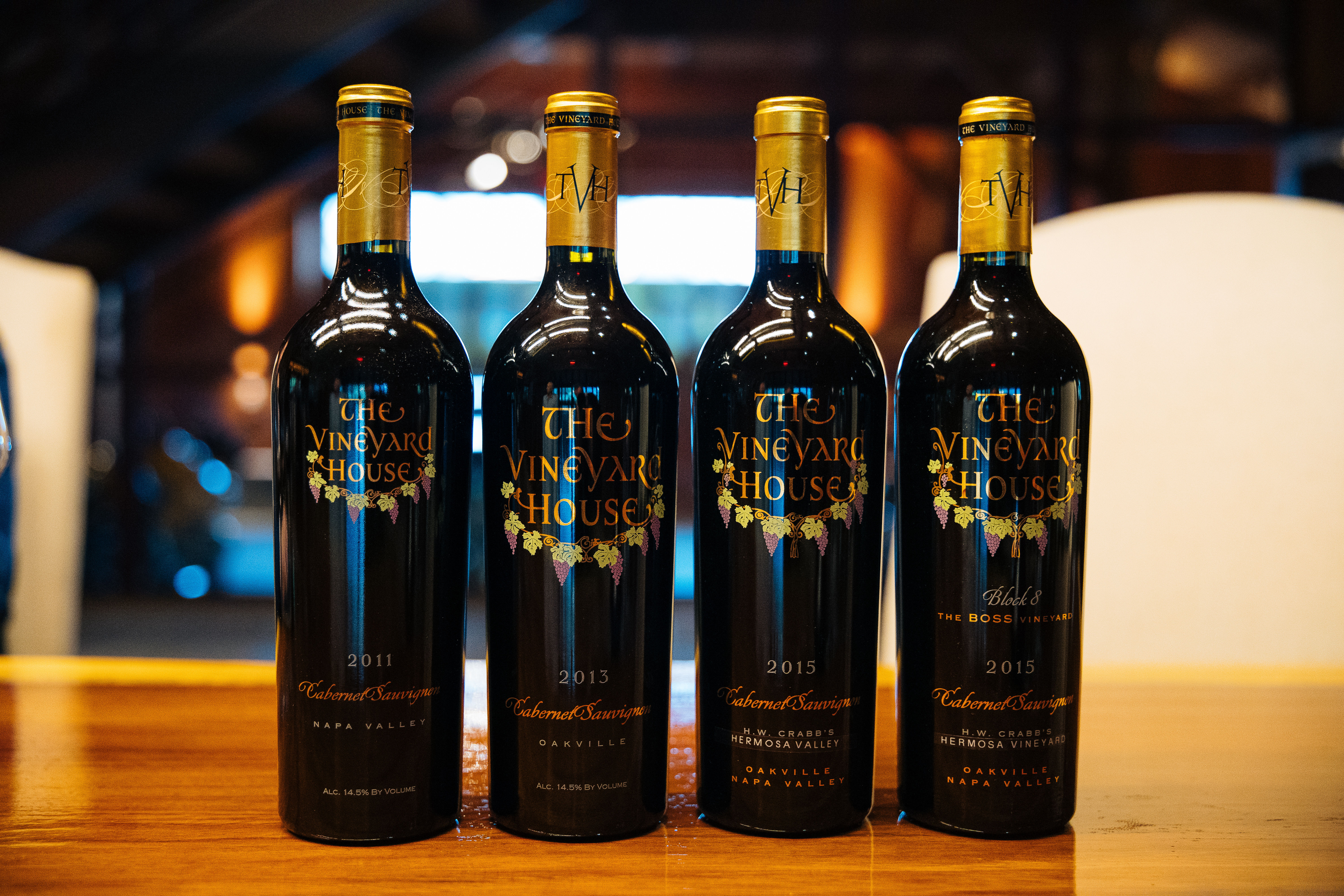 Four bottles of red wine with gold tops, with 'The Vineyard House' on the label