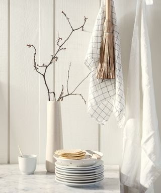 A white wall with towels hanging and a vase with branches