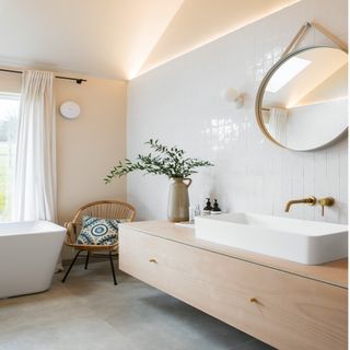 bathroom with white bath and basin, wooden drawers, white tiles and wicker chair