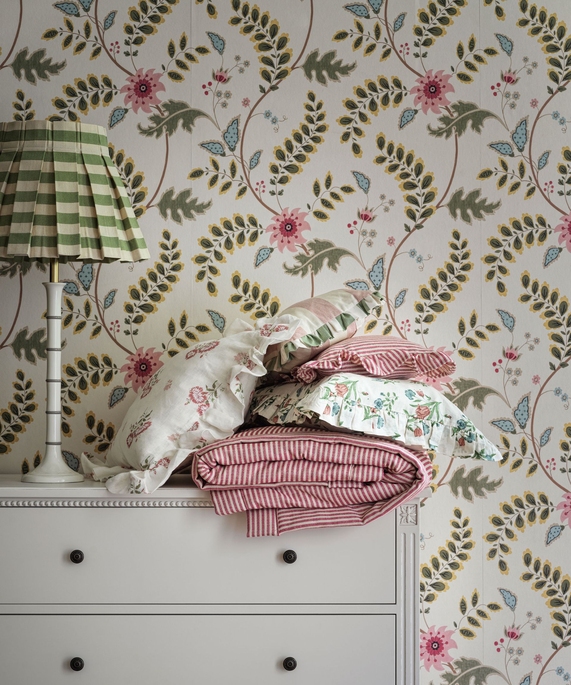 Floral wallpaper, white table lamp with green and white striped shade.