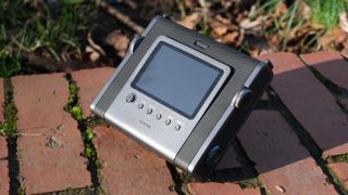 Fujifilm Instax Wide Evo sat on a red brick wall in the sun