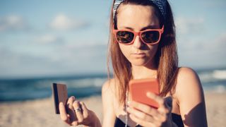 Woman on the beach looking at her phone and credit card