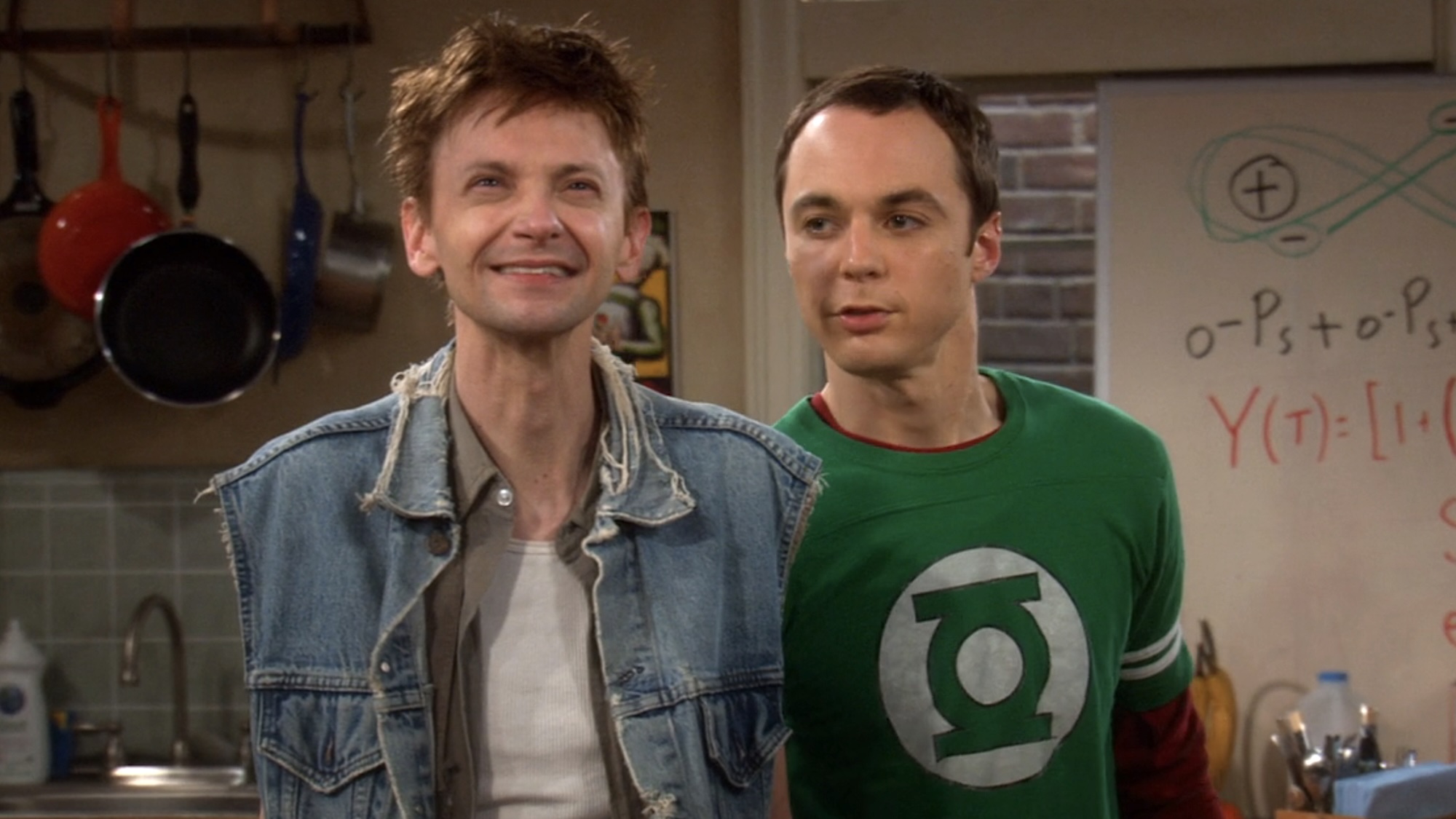 Jim Parsons' Sheldon Cooper in Green Lantern T-shirt side-talking into the left ear of DJ Qualls' Toby Loobenfeld wearing sleeveless denim jacket and white undershirt, on The Big Bang Theory Season 1