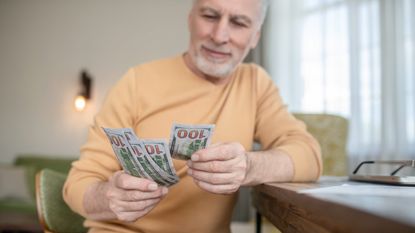 A gray-haired man counts $100 bills.