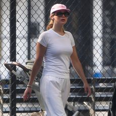 Jennifer Lawrence wears white top and bottoms with gray adidas and a baseball cap. 