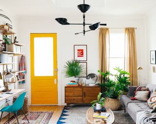 An open plan living room with yellow front door, two rugs on wooden floor, low grey sofa and coffee table and office area with modular shelving