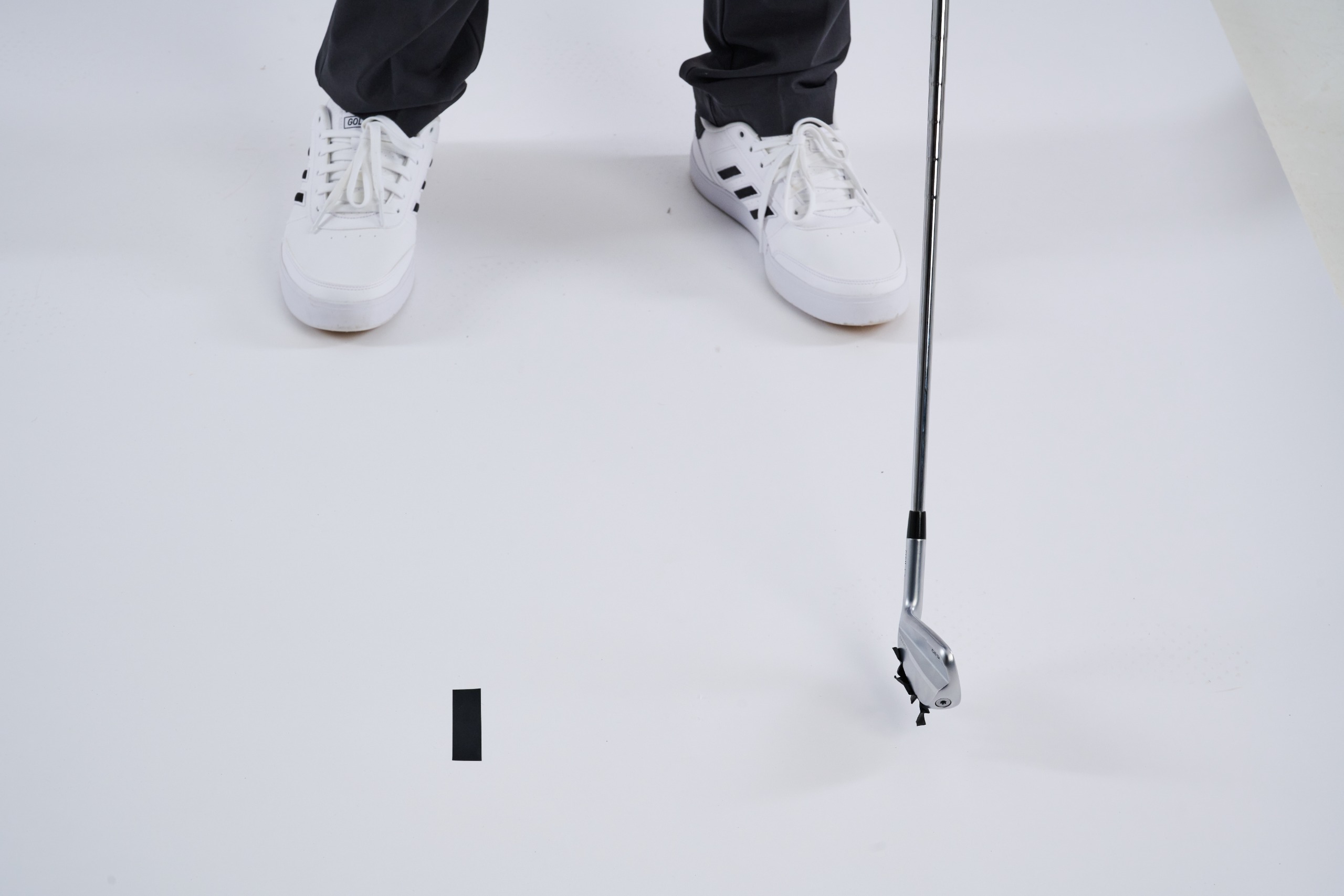 Two pieces of tape stuck to the bottom of the club after impact, with one remaining piece of tape on the ground unaffected