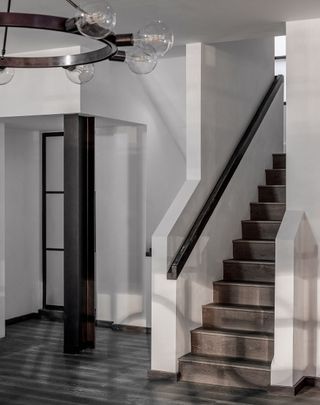 Staircase with white walls and brown tiles with a pendant light hanging above it.