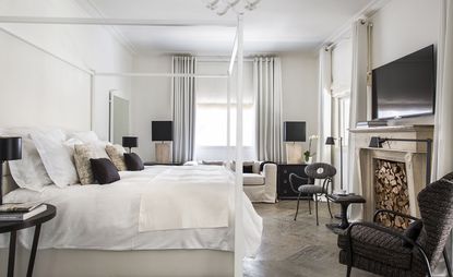 Bedroom with framed base, white linen, dark spotted single chairs and small coffee table infront of fireplace and above television